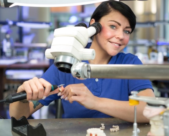 Smiling lab technician crafting a dental restoration
