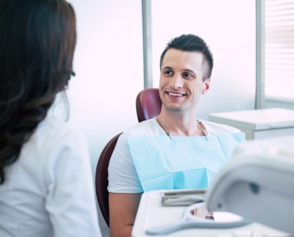 Man in dental chair smiling at dentist after receiving dental restoration crafted in local dental lab